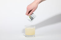 BRDY JUICE electrolyte powder dissolving into golden iced tea lemonade in a glass — the transformation moment