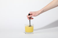 Hand stirring golden iced tea lemonade electrolyte drink made from BRDY JUICE powder in a clear glass